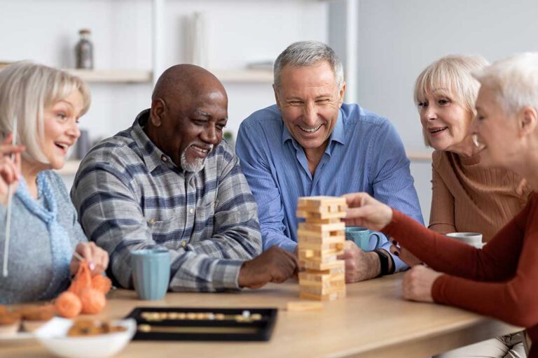 Staff member reviews a medication chart beside an older resident seated at a dining table.